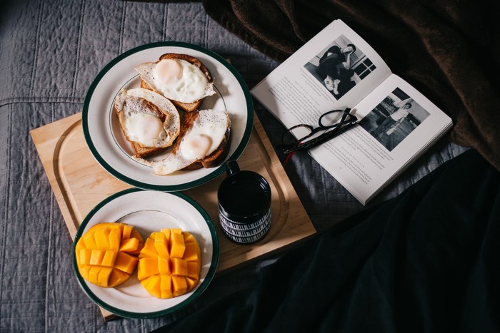 Breakfast in bed with fried eggs, mango, and a book