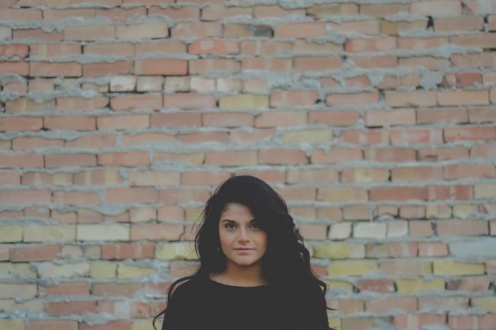 Woman with long black hair in front of a brick wall