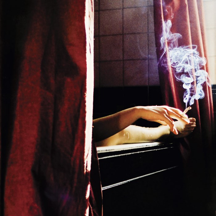 Woman smoking in a bathtub behind a curtain