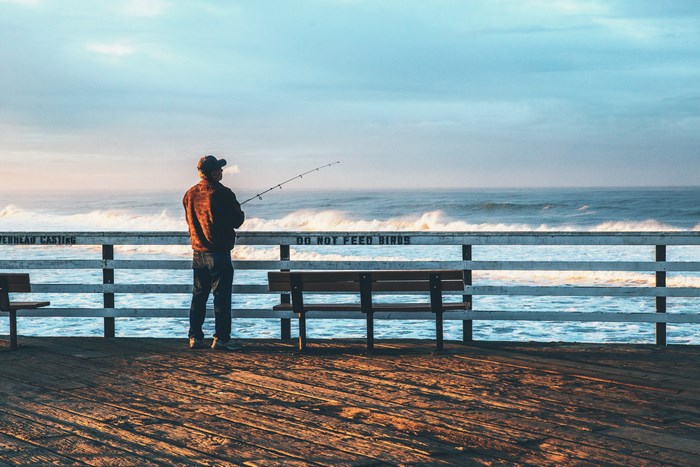 Fisherman on a pier casting a line into the ocean