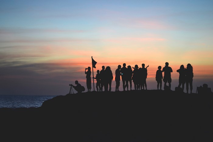 Group of people silhouetted against a sunset over the ocean