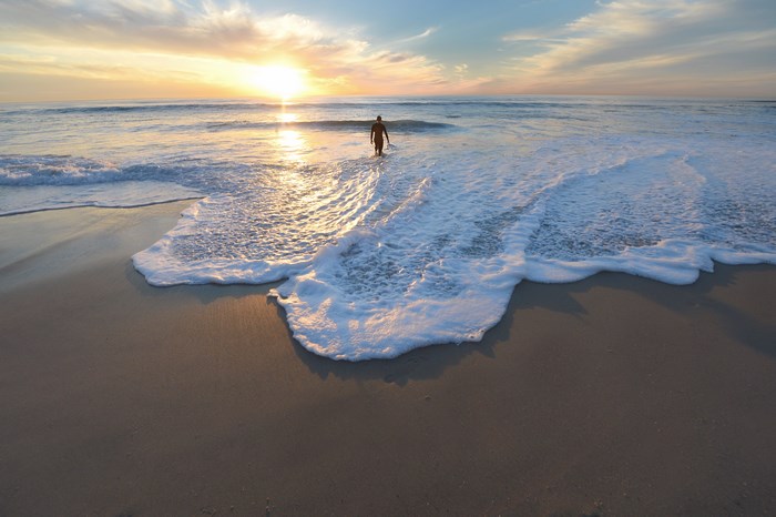 Man walking into the ocean at sunset