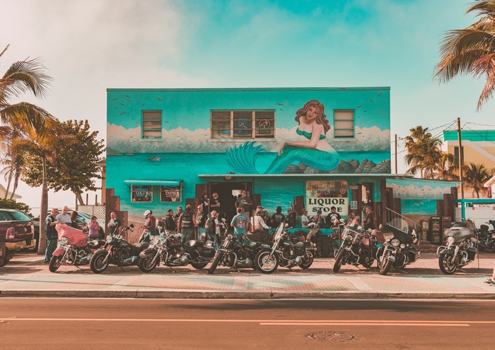 Motorcycles parked outside a liquor store with a mermaid mural