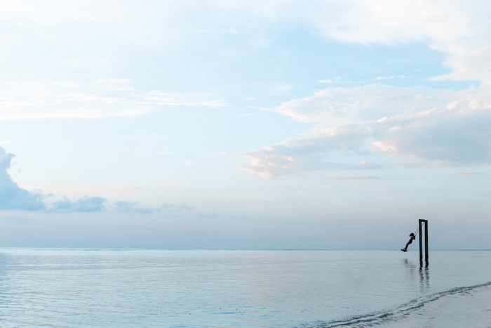 Person on a swing in the calm sea under a cloudy sky
