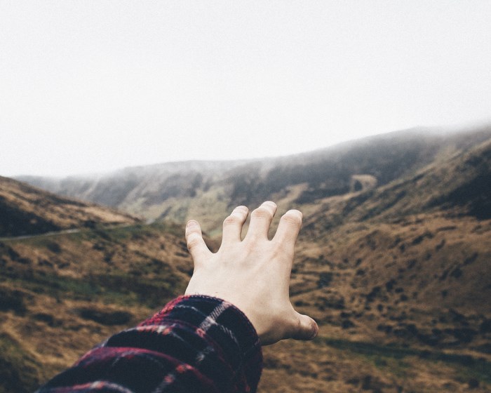 Hand reaching out towards misty mountains