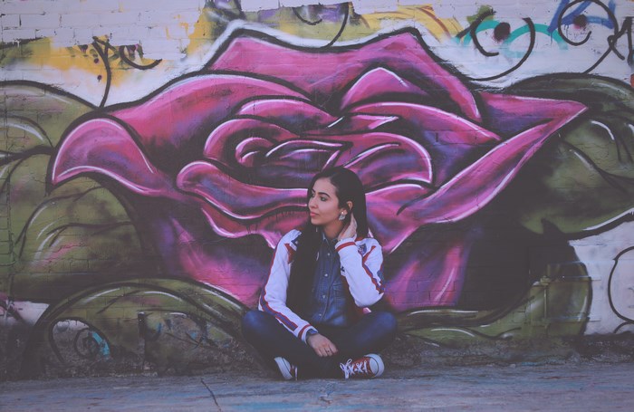 Woman sitting in front of a large rose graffiti