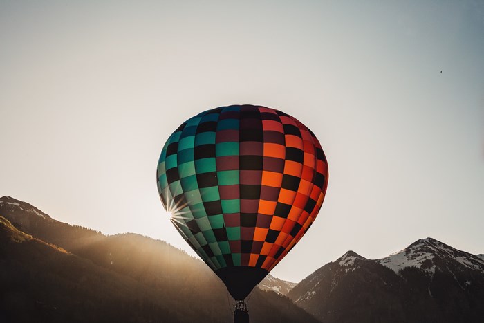 Hot air balloon flying over mountains at sunrise