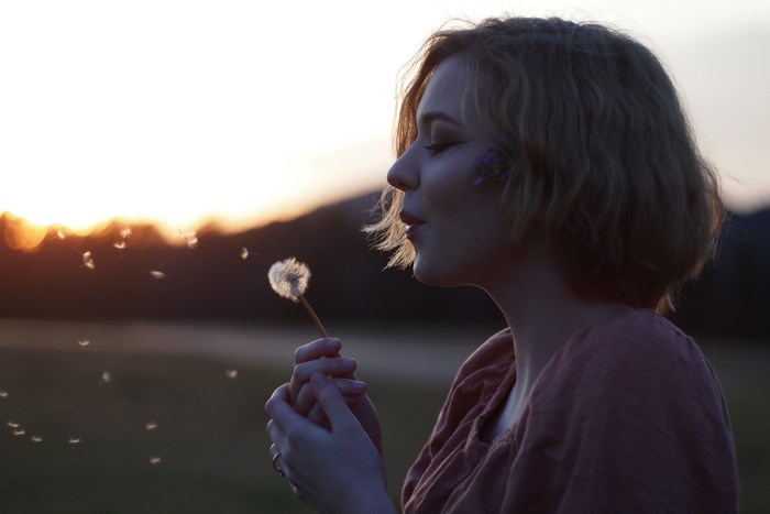 Woman blowing dandelion seeds at sunset