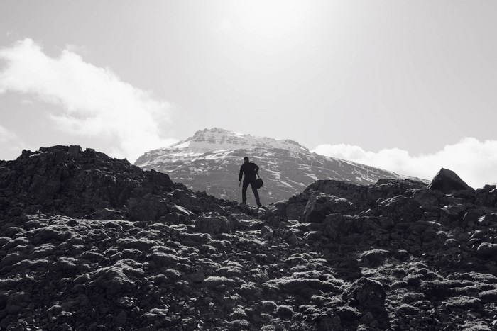 Man climbing a rocky mountain under a cloudy sky