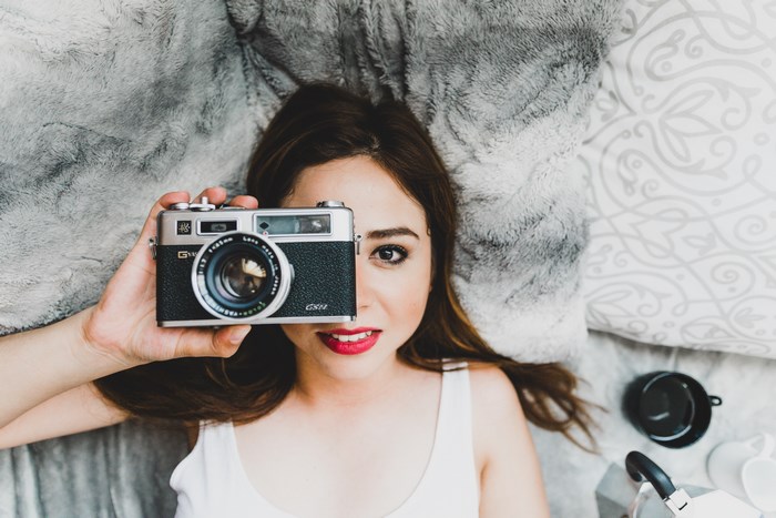 Woman holding a vintage camera on a bed