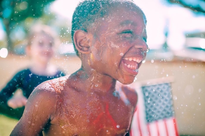 Boy laughing while being sprayed with water near American flag