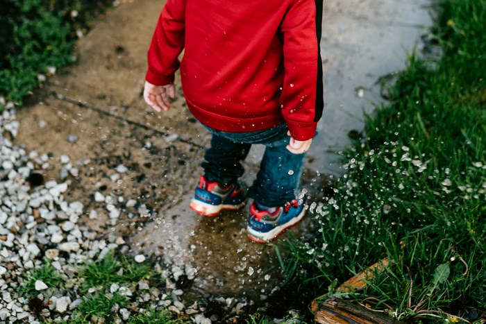 Child in red sweatshirt jumping in a puddle