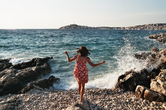 Woman in dress running into the sea on a rocky shore