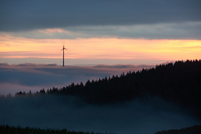 Wind turbine in fog at sunrise over a forest