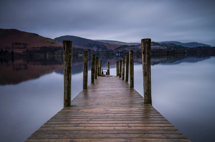Wooden dock with poles on a calm lake with hills
