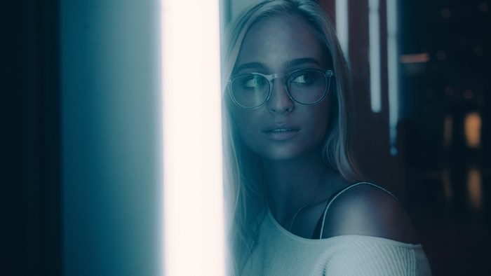 Woman with blonde hair wearing glasses near blue light