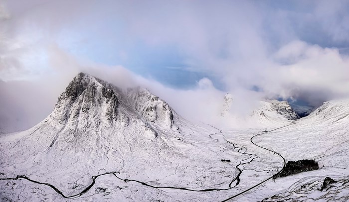 Snowy mountain valley with a winding road and clouds