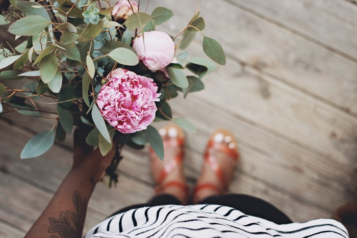 Person holding a pink peony bouquet on wooden flooring