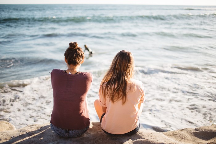 Two friends sitting on rocks by the ocean