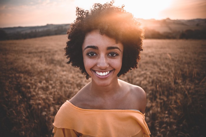 Young woman smiling in a field at sunset