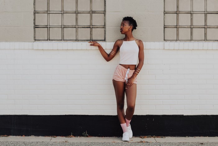 Woman in pink shorts and white top posing by brick wall