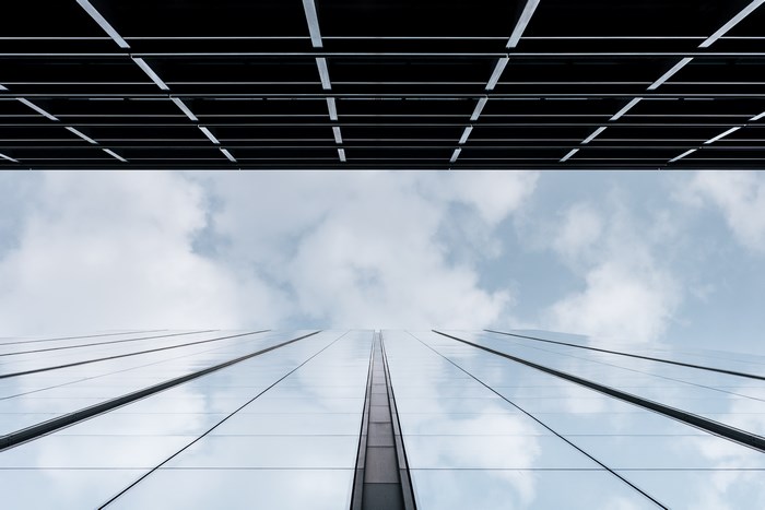 Low angle view of a modern glass skyscraper against a cloudy sky