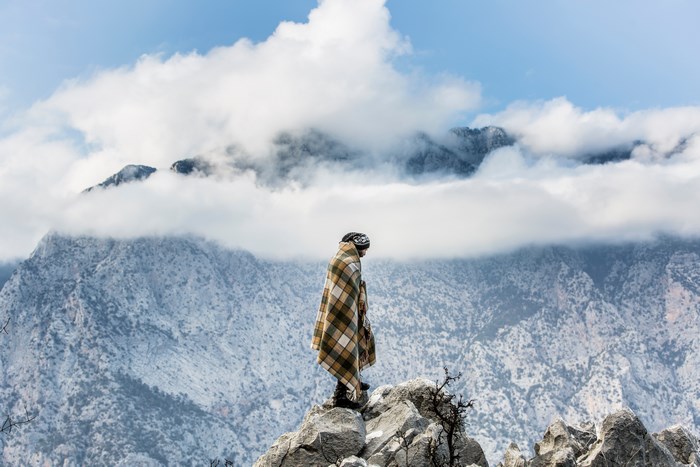 Man wrapped in blanket on mountain peak with clouds