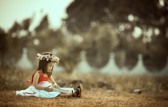 Girl with flower wreath reading a book outdoors