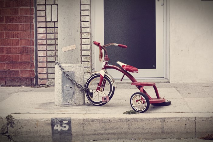 Red tricycle chained to a pole on a sidewalk
