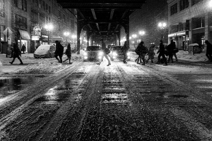 People walking on a snowy street at night under a bridge