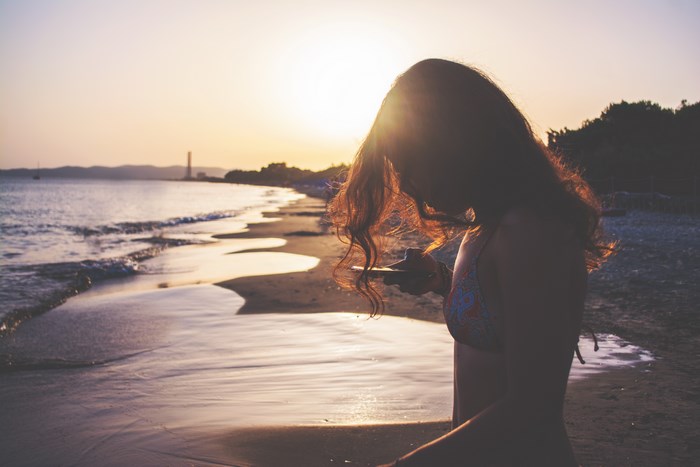 Woman in bikini using phone on beach at sunset