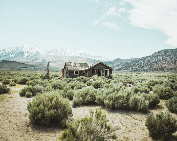 Abandoned cabin in a desert valley with snowy mountains