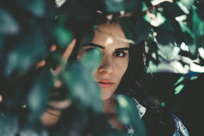 Woman peeking through green leaves in nature