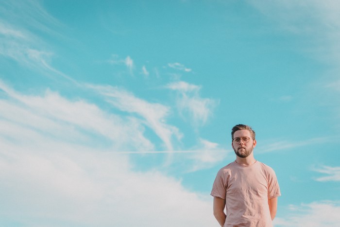 Man with beard and glasses in a pink t-shirt against blue sky