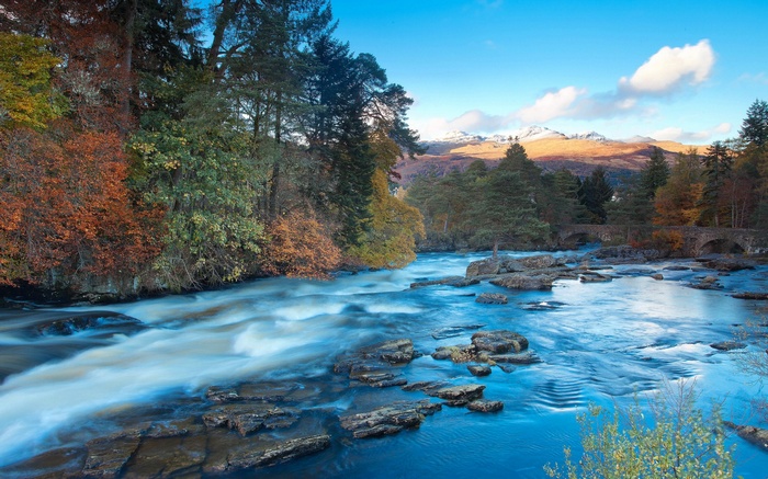 River flowing through autumn forest with snow-capped mountains
