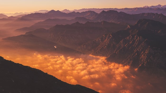 Paraglider over orange clouds in Italian mountains at sunset