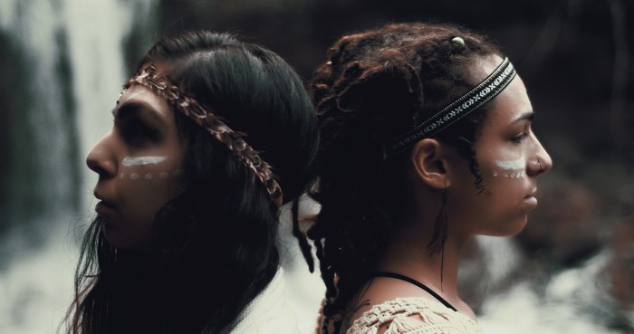 Two women with face paint and headbands by a waterfall