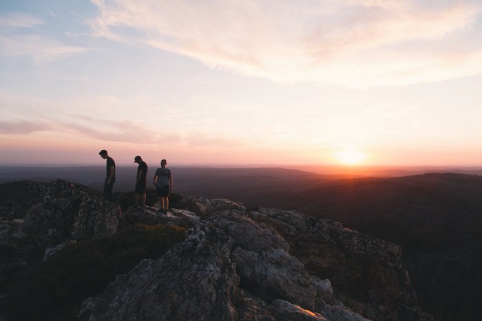 Three men on a rocky cliff at sunset