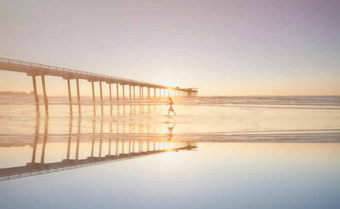Woman walking on beach near pier at sunset