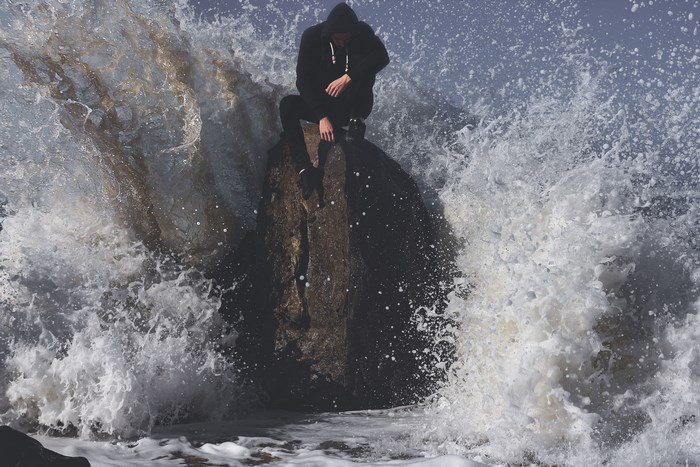 Man in hoodie sitting on a rock in the ocean