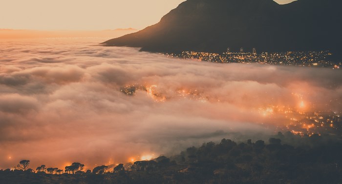 City lights shrouded in fog at sunset with mountain silhouette