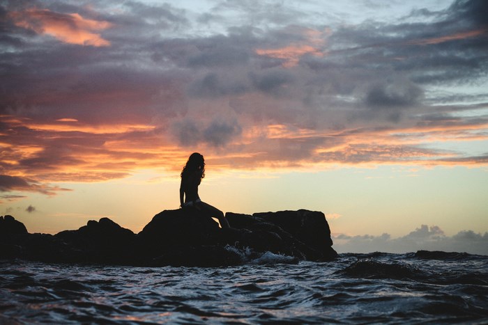 Silhouette of a woman sitting on rocks at sunset