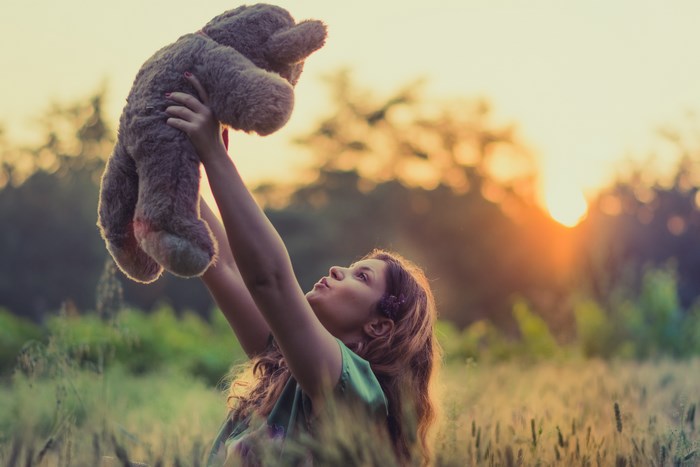Girl holding a teddy bear at sunset
