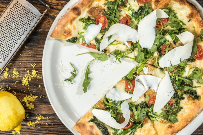 Pizza with arugula, tomatoes, and shaved parmesan on a plate