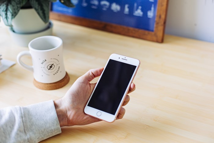 Person holding an iPhone on a wooden desk with a mug