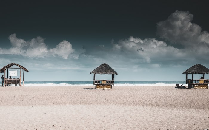 Beach huts on the sand with ocean waves and clouds
