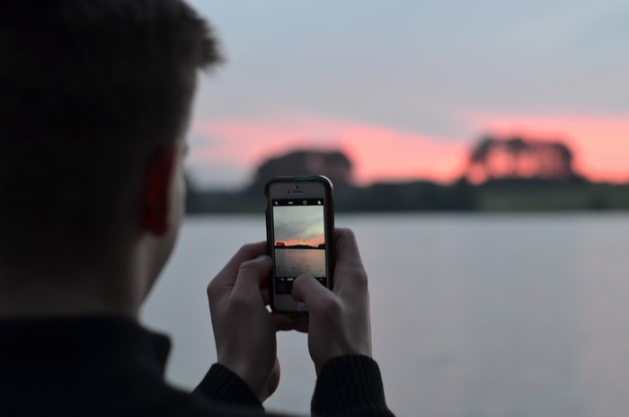 Person taking a photo of a sunset over a lake with an iPhone