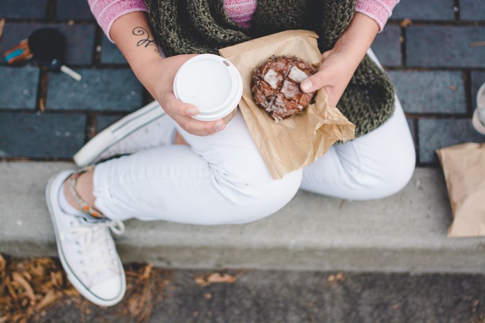 Woman holding a donut and coffee cup