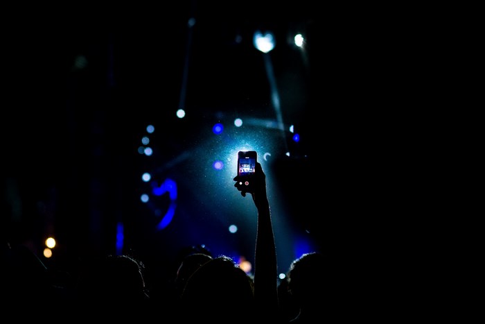 Person holding smartphone at a concert with spotlights