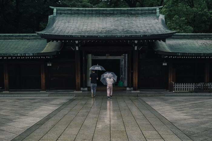 Two people with umbrellas walk towards Meiji Jingu shrine in Tokyo